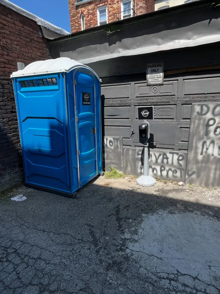 Blue construction porta potty placed beside a building in an alley